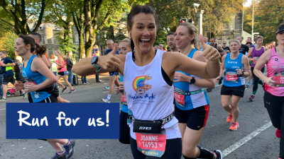 ID: A photo of a lady waving at the camera in front of a crowd of runners at the Cardiff Half Marathon in a Noah's Ark Charity vest top.